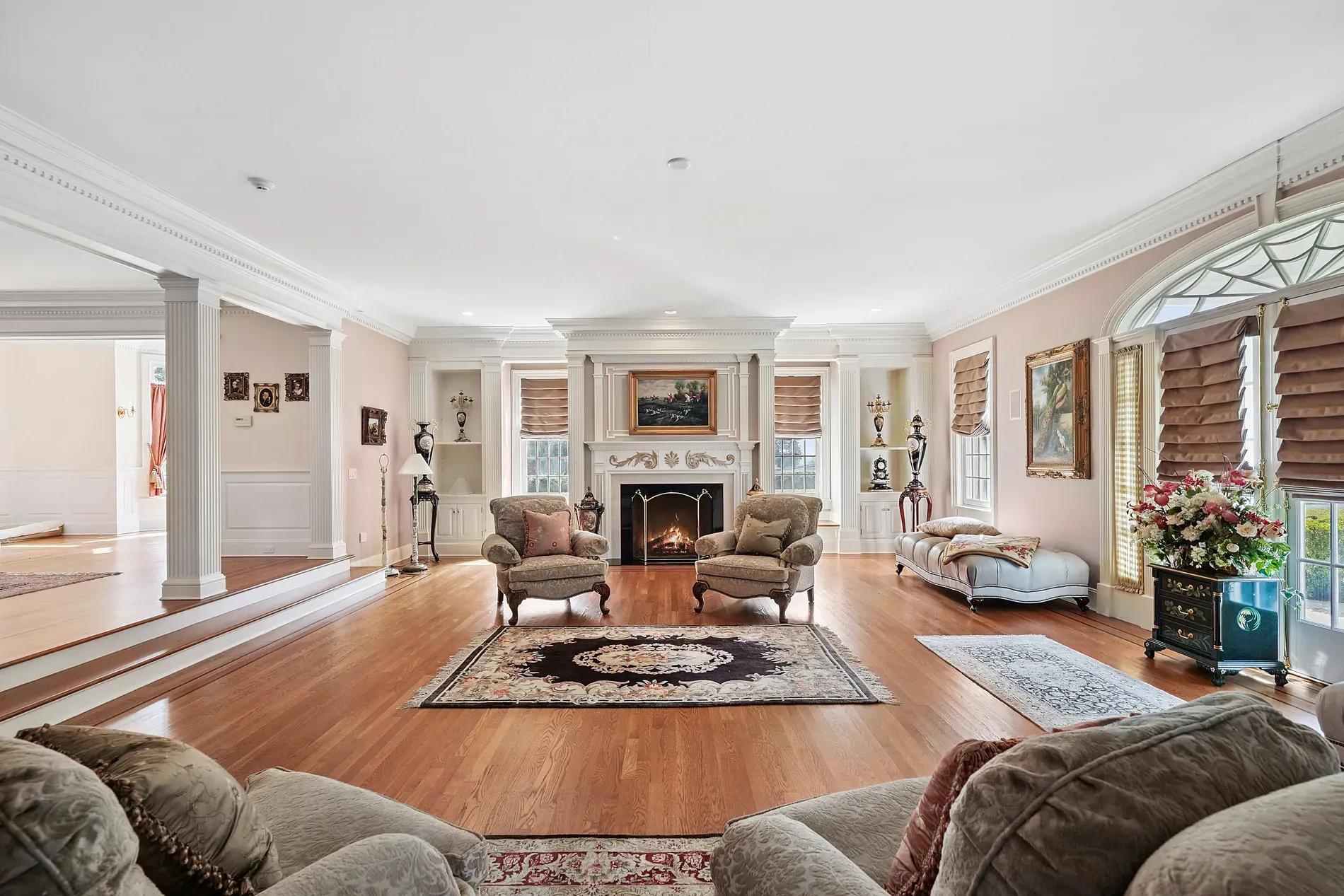 Big living room energy — beige walls, rich wood floors, plush center sofa zone.