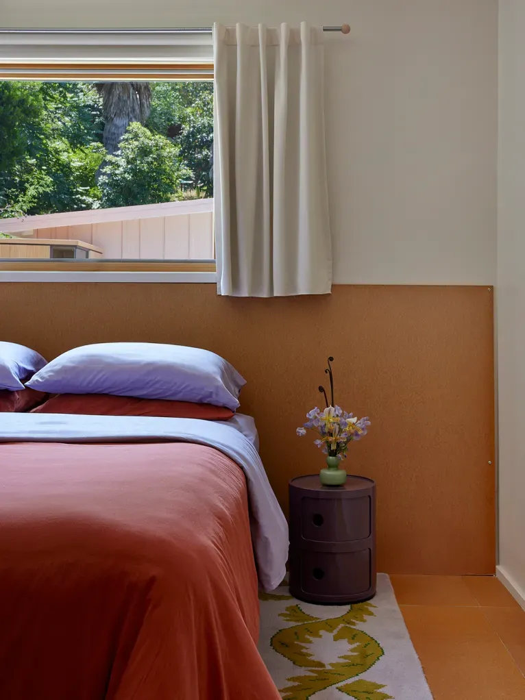 Here's the bedroom — rust duvet, white pillows, warm walls. Cozy without trying.