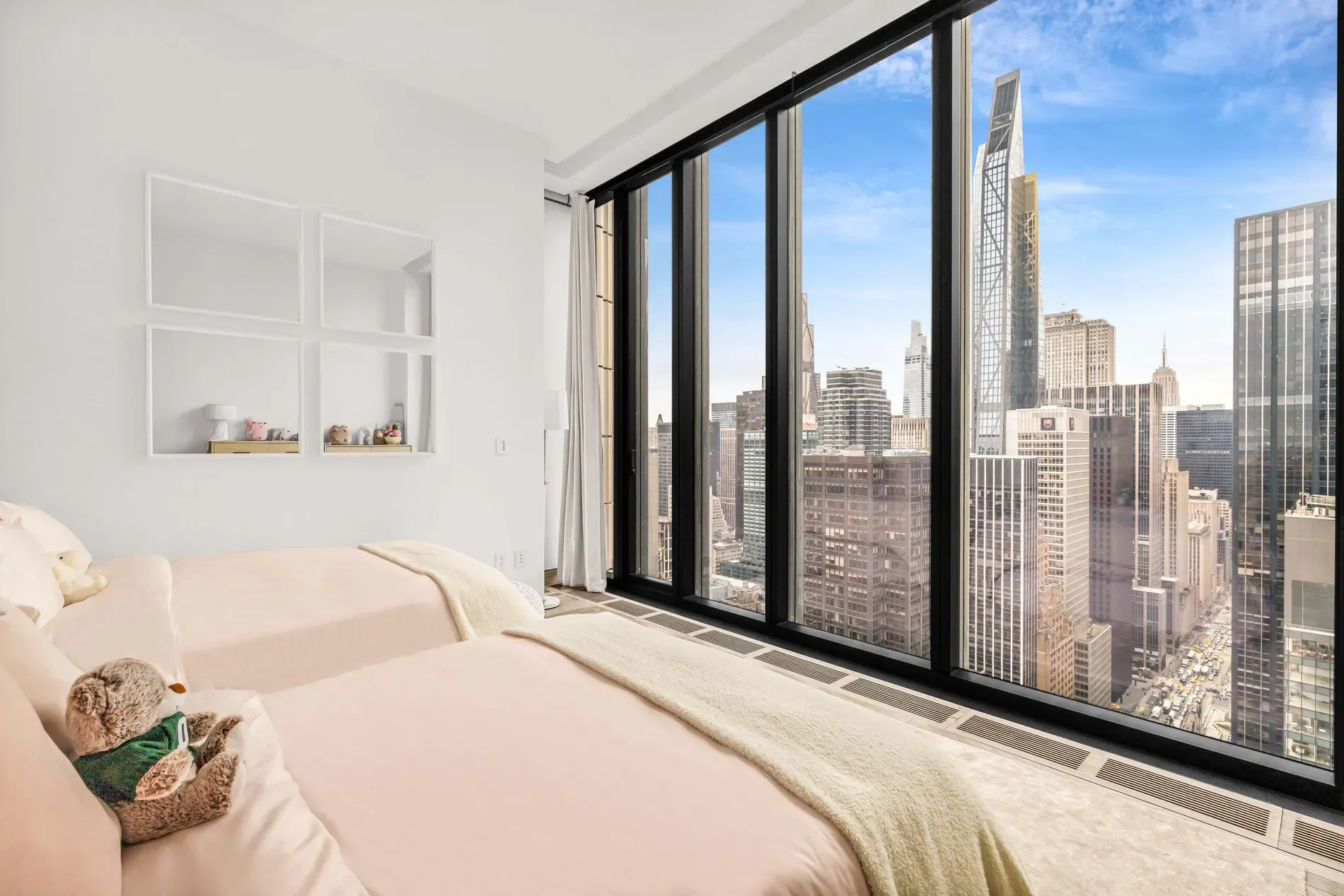 Bedroom one — wall of glass, beige linens, city doing all the work.