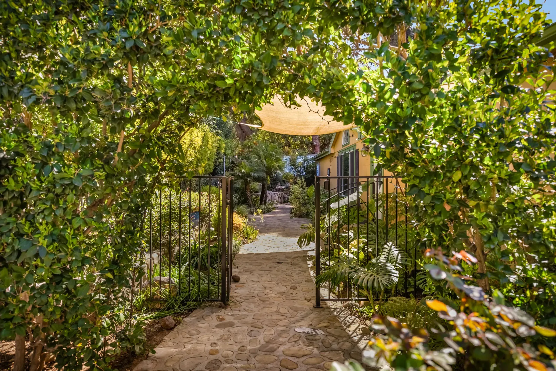 Green-covered archway over a wavy cobblestone path. Fairytale entrance energy.