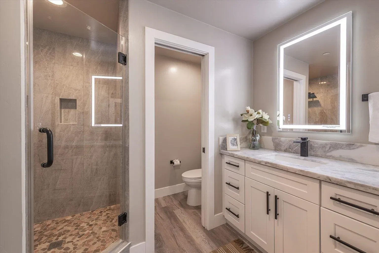 Glass shower glistening on the left. everything else calm greys and white.