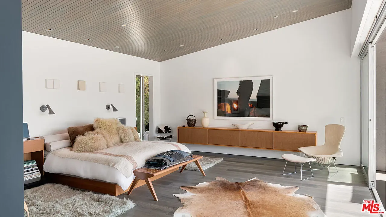 Minimal bedroom with layered textures. Neutral bedding, warm wood, very calm.