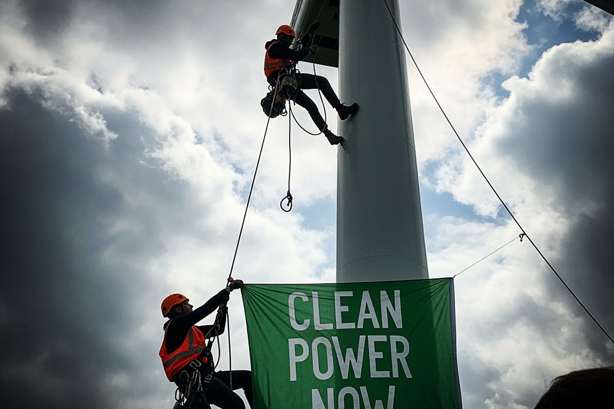 A large banner with an environmental slogan being unfurled from a wind turbine