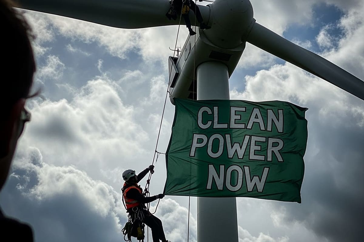 A person in climbing gear ascending a wind turbine blade against a stormy sky