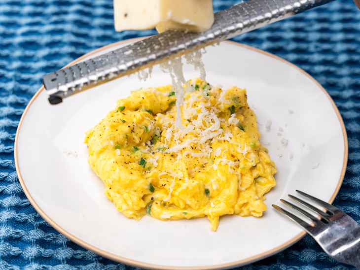 Oprah Winfrey's truffle scrambled eggs on a plate with someone grating cheese over the top