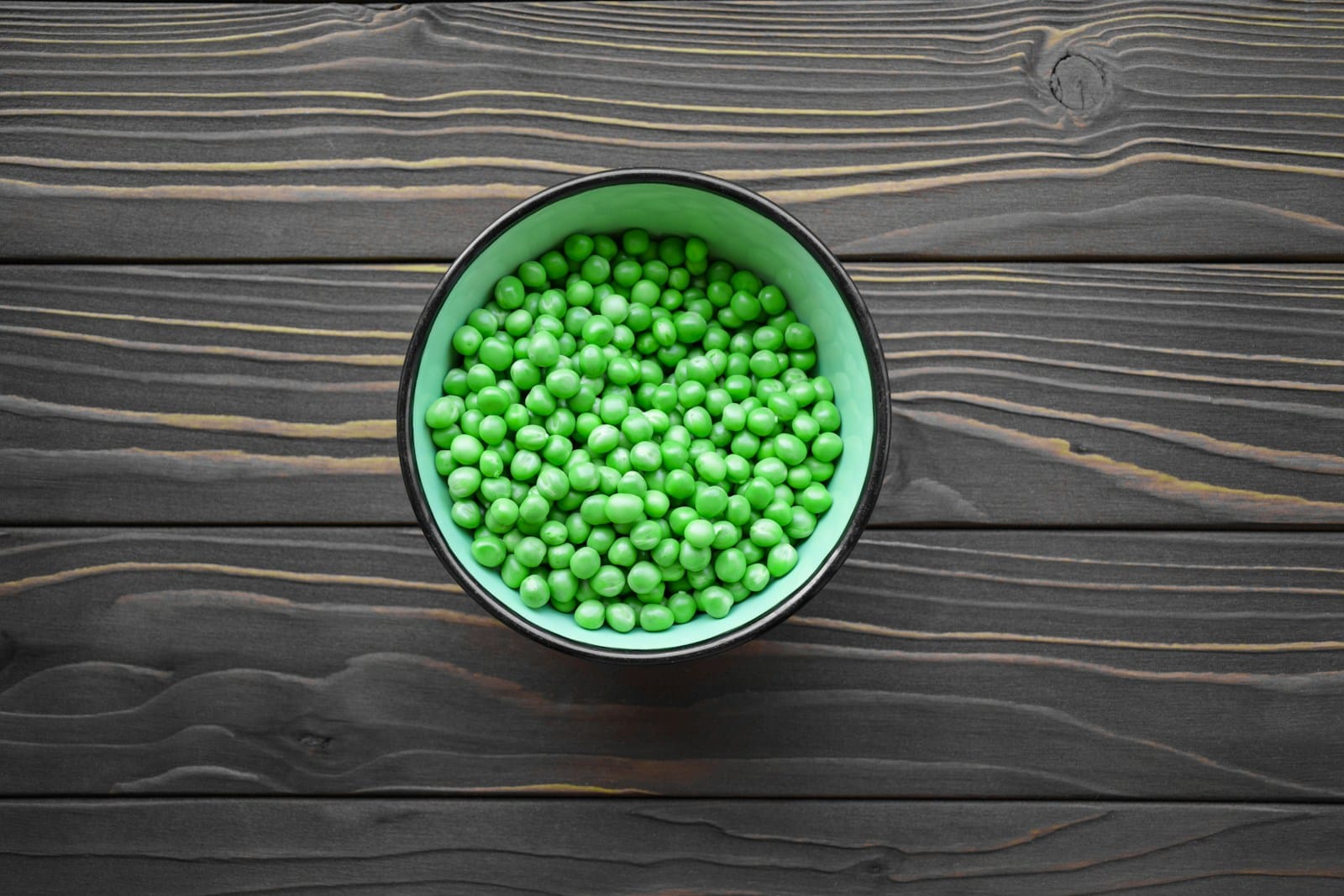 a green bowl filled with peas on top of a wooden table