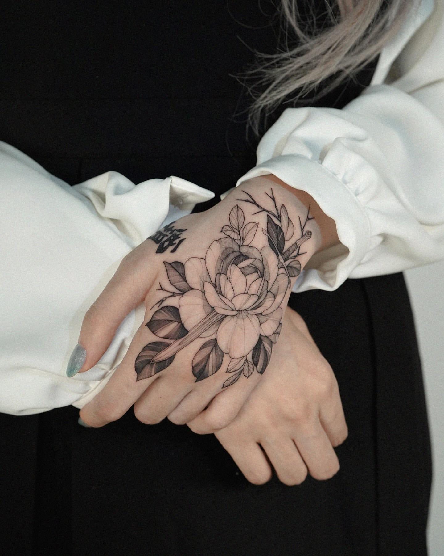 Delicate line work transforms this hand into a living canvas, where an intricate peony blooms across the palm with stunning botanical detail. The strategic placement means this floral masterpiece can be revealed or concealed at will, making every gesture a work of art. Black ink shading brings depth to each petal and leaf, creating a tattoo that's both bold and beautifully feminine 🌸