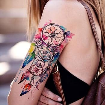 Cascading down the upper arm like a bohemian waterfall, this dreamcatcher tattoo bursts with jewel-toned splashes that transform traditional black ink into pure artistry ✨ The intricate web of circles and feathers creates a mesmerizing flow, while pops of coral, turquoise, and golden yellow breathe life into every sacred symbol. A perfect fusion of spiritual meaning and stunning watercolor technique that turns skin into a canvas of dreams.