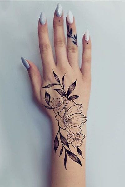 Delicate botanical artistry flows across the hand and wrist in this stunning black ink design, featuring graceful flowers and leaves that seem to dance with natural movement. The strategic placement creates an elegant extension of the body's natural lines, while the fine linework and organic curves showcase masterful tattoo craftsmanship 🌸 Perfect for those who want their ink to feel like wearable art!