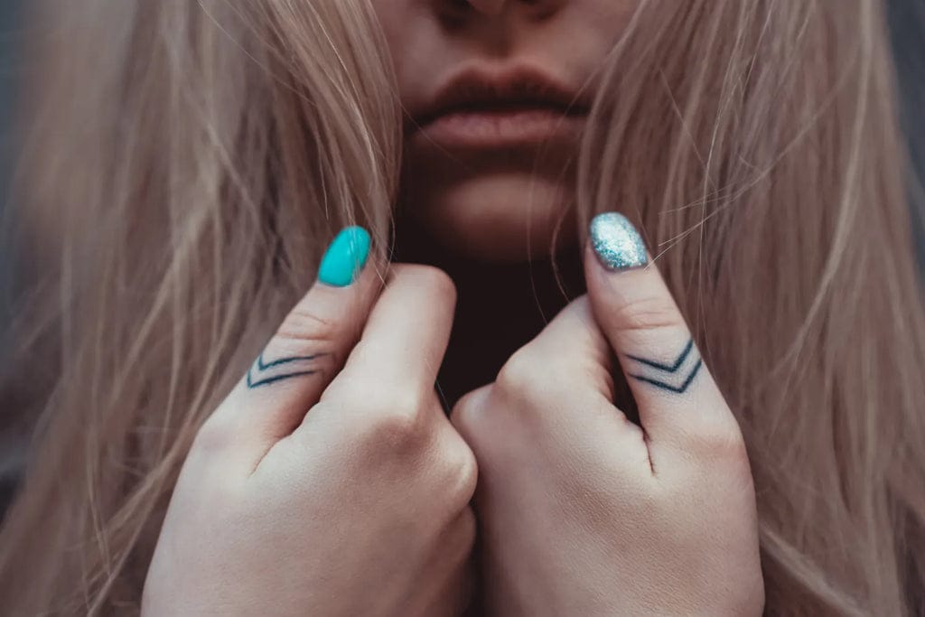Geometric chevron lines dance across knuckles like minimalist arrows pointing toward endless possibilities ✨ The crisp black ink creates striking contrast against pale skin, while those perfectly painted teal nails add an unexpected pop of color that makes the whole look absolutely captivating. Simple yet profound, these finger tattoos prove that sometimes the smallest details make the biggest statement.