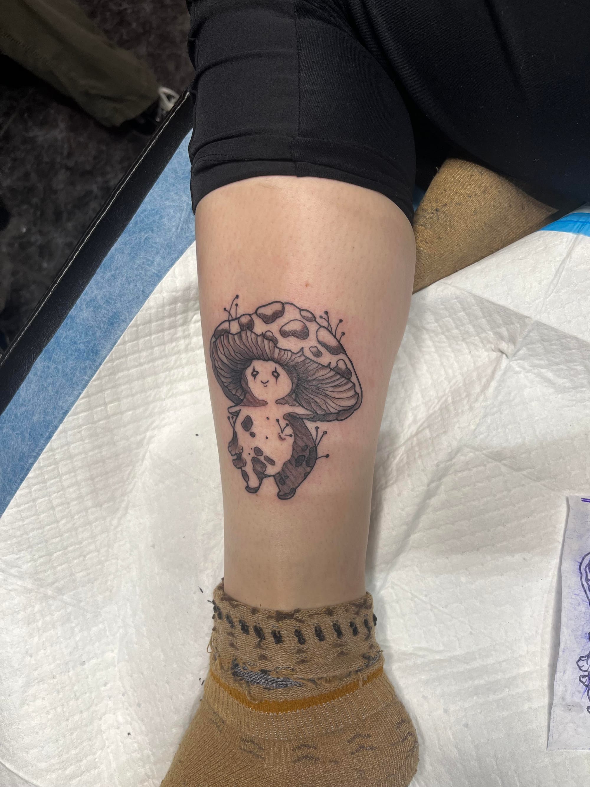 Whimsical meets wonderful in this adorable mushroom character tattoo that transforms the calf into a canvas for cottagecore dreams. The sweet spotted fungi sports the most endearing little face and delicate botanical details, creating a perfect blend of cute and nature-inspired ink. 🍄 Black line work keeps the design clean while the charming personality shines through every carefully crafted detail.
