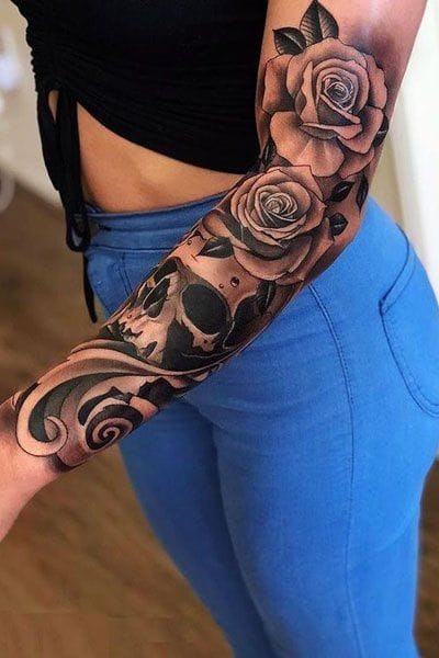 Dramatic black and gray realism transforms this entire forearm into a stunning botanical masterpiece, where detailed roses bloom alongside mysterious skull imagery and ornate scrollwork. The seamless flow from shoulder to wrist creates an incredible sleeve that perfectly balances feminine florals with darker gothic elements 🖤