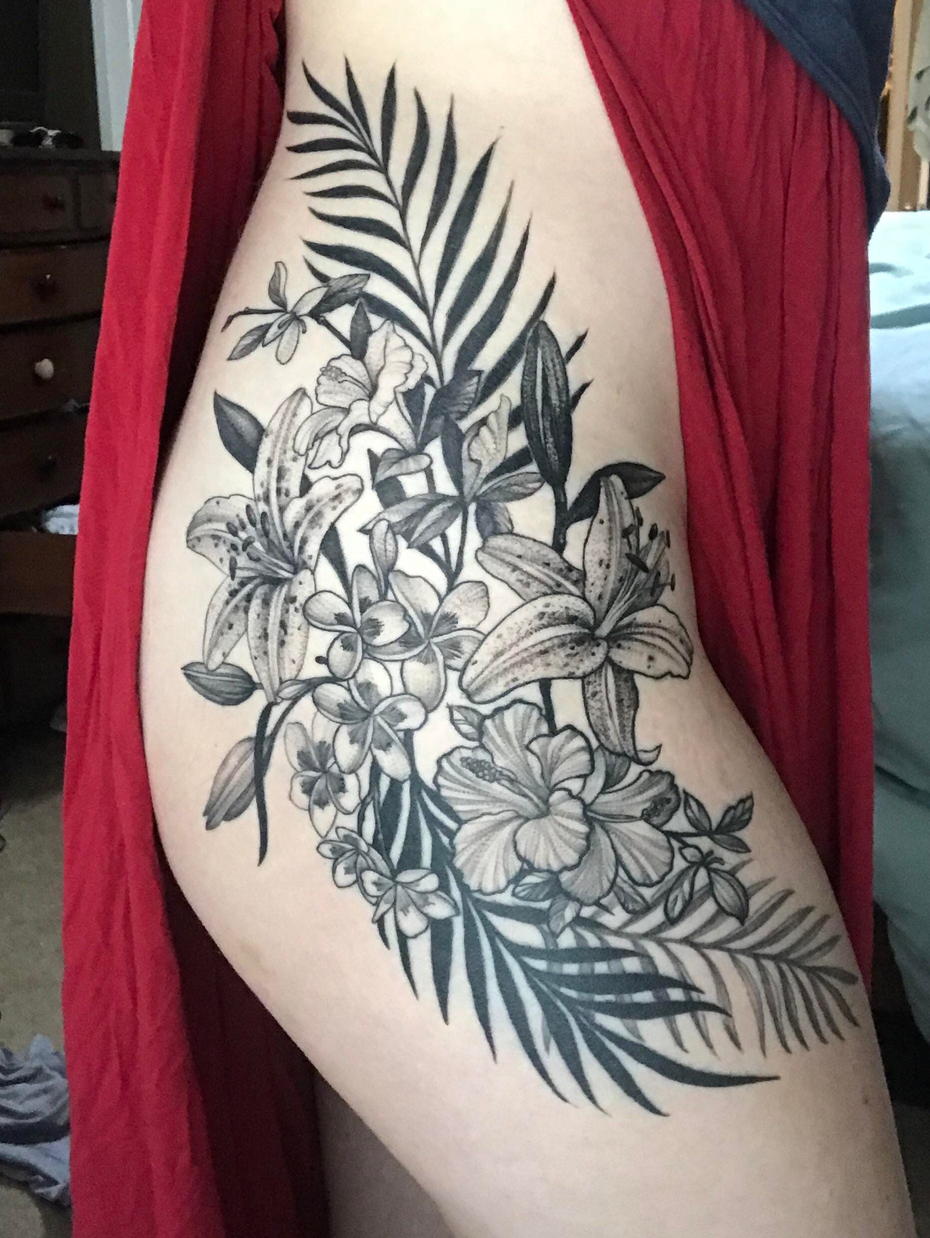 Botanical artistry blooms across this stunning thigh piece, where delicate lilies intertwine with tropical palms and plumeria in exquisite black and grey detail. The flowing composition creates natural movement down the leg, showcasing the artist's masterful shading technique that brings each petal and leaf to life with remarkable depth and dimension. 🌺