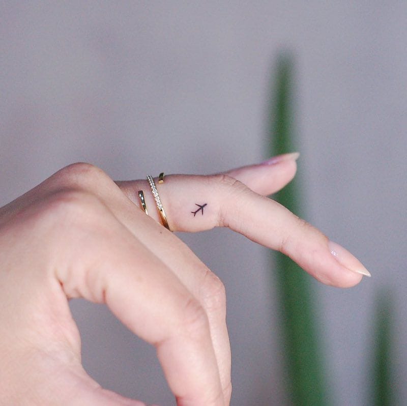 Wanderlust takes flight on delicate skin with this minimalist airplane silhouette gracing the finger. The simple black linework creates an elegant contrast against the gold stacked rings, transforming everyday hand gestures into subtle reminders of adventure and freedom ✈️