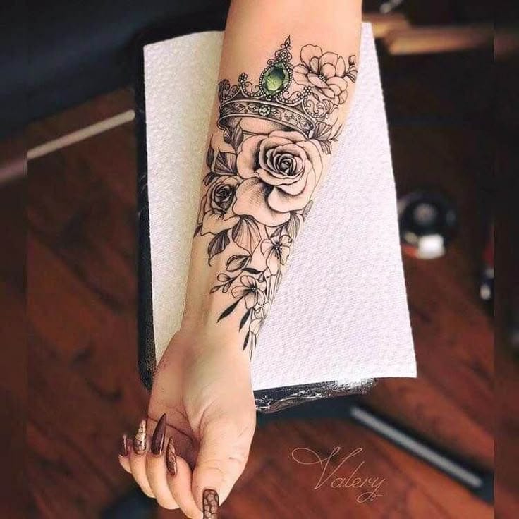 Delicate florals cascade beneath an ornate crown in this stunning forearm piece that perfectly balances regal elegance with feminine grace. The intricate linework and subtle shading create beautiful depth, while that pop of emerald green in the crown's centerpiece adds just the right amount of color contrast 👑 A truly sophisticated design that flows beautifully with the natural curve of the arm.