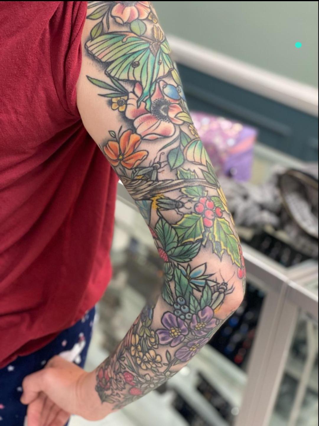 Nature's artistry blooms magnificently across this full sleeve, where delicate botanical elements dance together in a symphony of soft pastels and vibrant greens. The intricate layering of flowers, leaves, and organic motifs creates an almost dreamlike garden that seems to grow naturally around the arm. Each petal and vine flows seamlessly into the next, showcasing masterful color blending that brings this living canvas to life 🌿