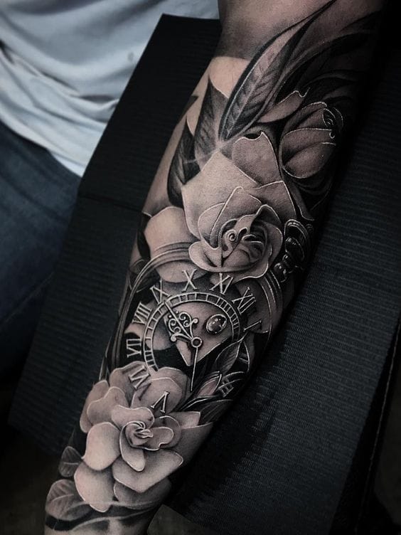 Dramatic black and grey realism transforms this forearm into a captivating narrative of time and beauty. The intricate pocket watch centerpiece, surrounded by blooming roses and delicate feathers, creates stunning depth through masterful shading techniques that make each element appear to float off the skin. ⏰🌹