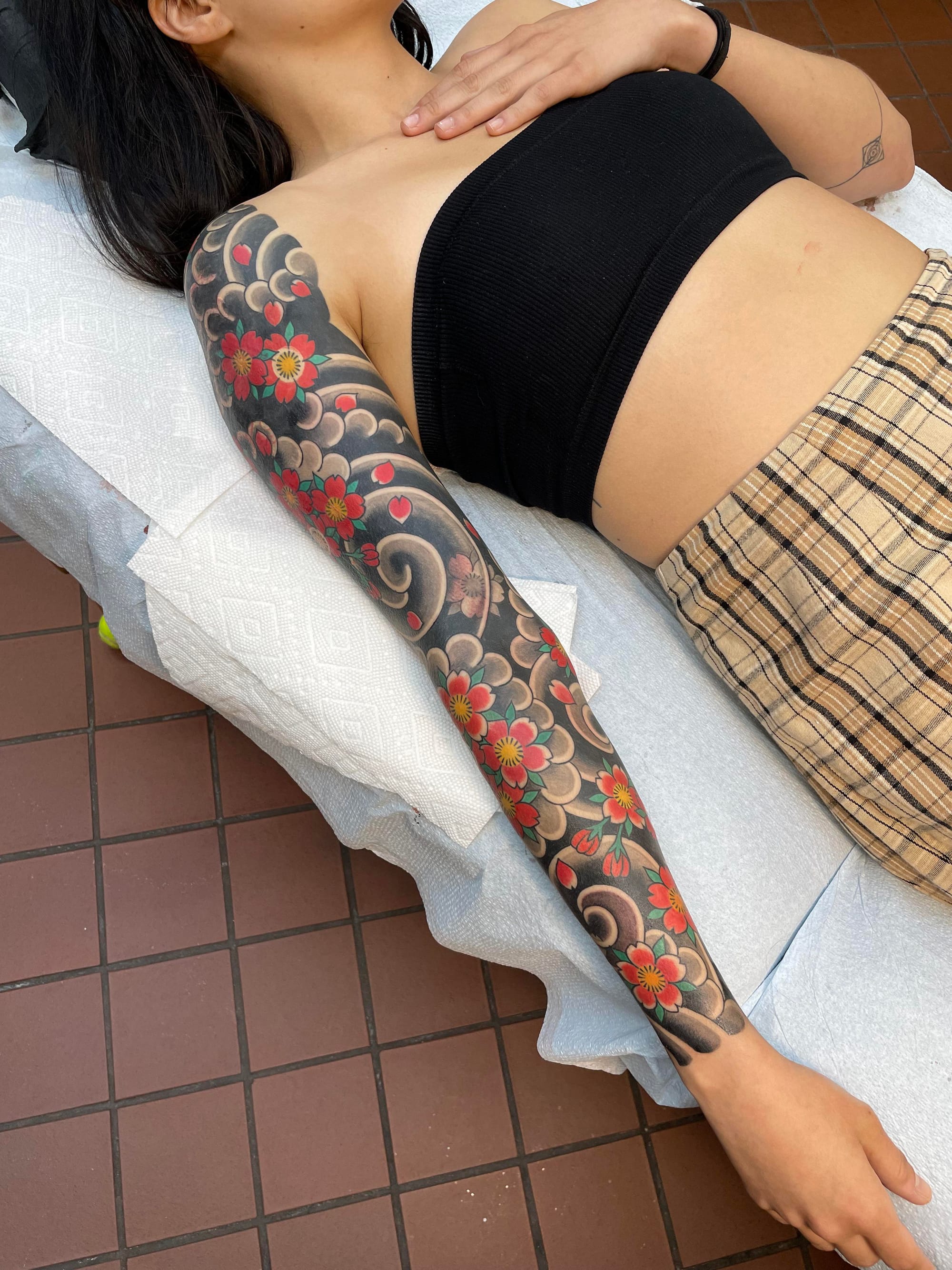 Cascading down this arm like a living garden, delicate cherry blossoms dance among traditional Japanese cloud motifs in rich coral and deep charcoal tones. The full sleeve placement creates a stunning canvas that flows seamlessly from shoulder to wrist, showcasing the intricate detail work that makes traditional Japanese tattooing so mesmerizing 🌸