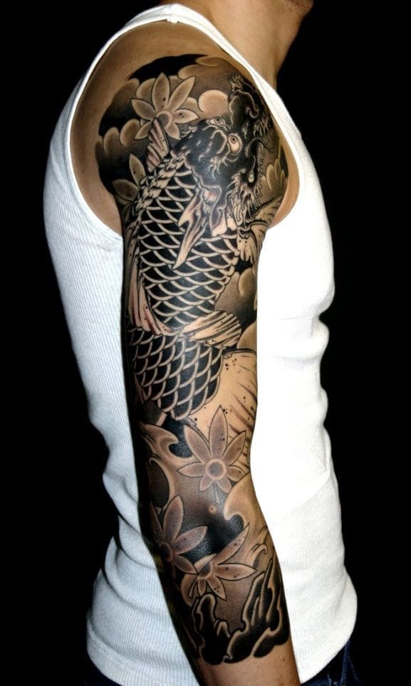 Masterful Japanese artistry transforms this entire arm into a living canvas, where an intricate koi fish swims through carefully detailed lotus blossoms and flowing water elements. The contrast between the rich black background and warm earth-tone shading creates incredible depth, making every scale and petal appear to move with lifelike precision 🐠 This sleeve demonstrates the pinnacle of traditional Japanese tattooing techniques with its seamless composition and flawless execution.