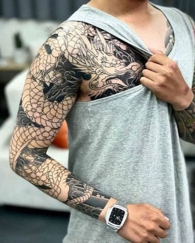 Serpentine elegance winds its way across this full sleeve masterpiece, where an intricately detailed dragon coils from shoulder to wrist in mesmerizing black and grey artistry. The scale work demonstrates exceptional technical skill, creating depth and movement that makes the mythical creature appear ready to slither right off the skin. A perfect example of how traditional Eastern dragon imagery can be modernized into contemporary tattoo excellence ✨