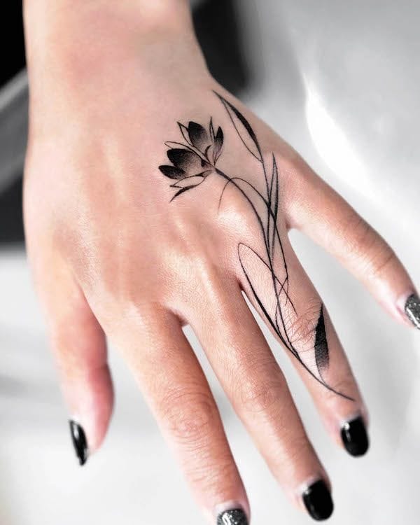 Delicate botanical artistry flows across knuckles and fingers in this stunning black ink design, featuring a graceful lotus bloom with trailing stems that follow the natural curves of the hand. The fine line work and strategic placement create an elegant piece that moves beautifully with every gesture 🌸 Perfect for those who want meaningful ink that's both subtle and striking.