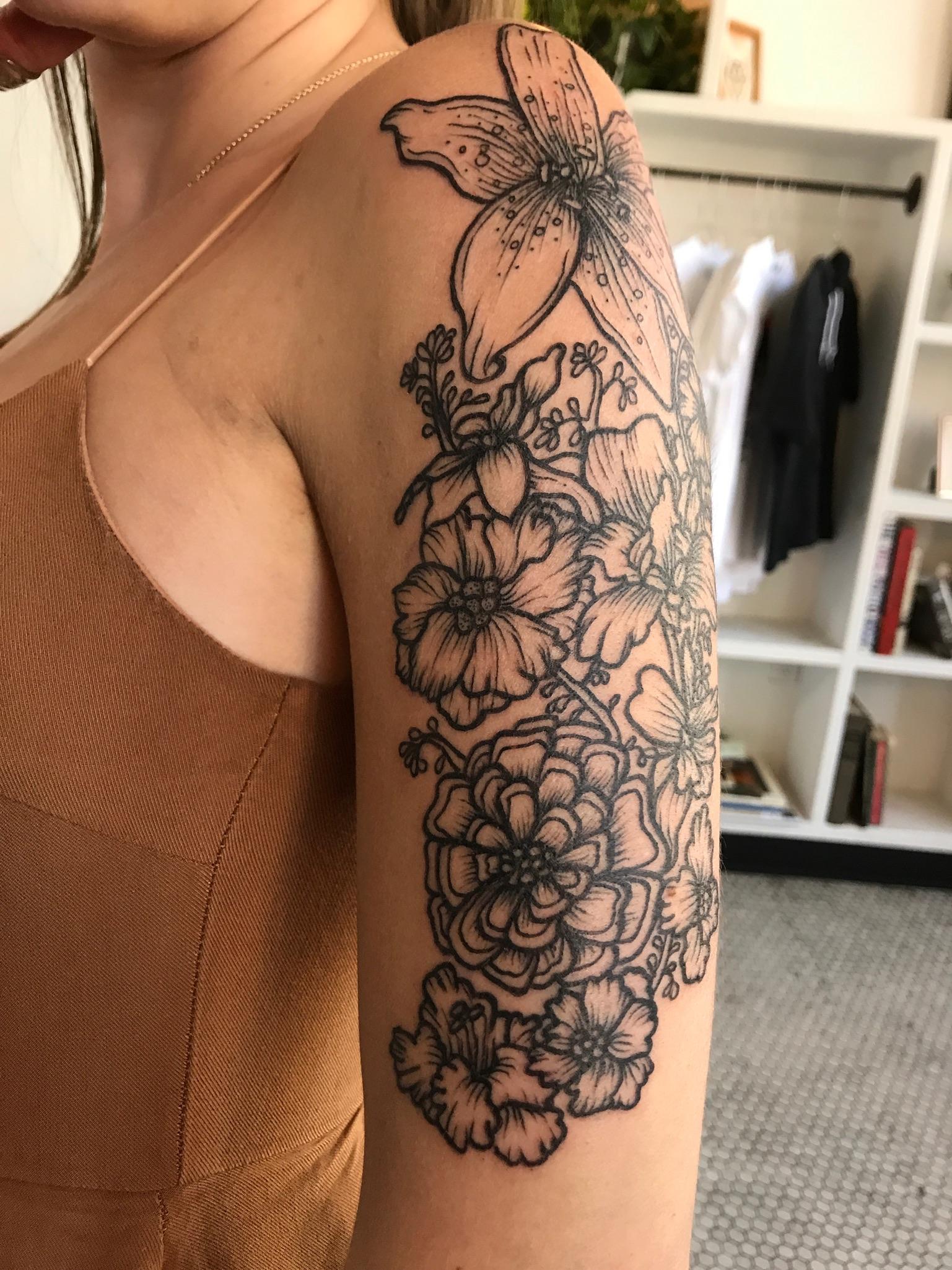 Botanical artistry blooms across this stunning half-sleeve, where delicate line work brings lilies, peonies, and wildflowers to life in gorgeous black ink. The flowing composition creates a natural garden that wraps beautifully around the arm, with each petal and stamen rendered in exquisite detail 🌸 Perfect inspiration for anyone dreaming of a feminine floral piece that celebrates nature's elegant beauty.