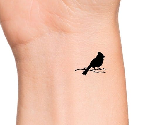Delicate simplicity meets profound symbolism in this minimalist bird silhouette, perched gracefully on a slender branch along the wrist's natural curves. The stark black ink creates a striking contrast against soft skin, while the small scale makes it feel like a whispered secret rather than a bold statement. Perfect for those who appreciate understated elegance with deeper meaning 🖤