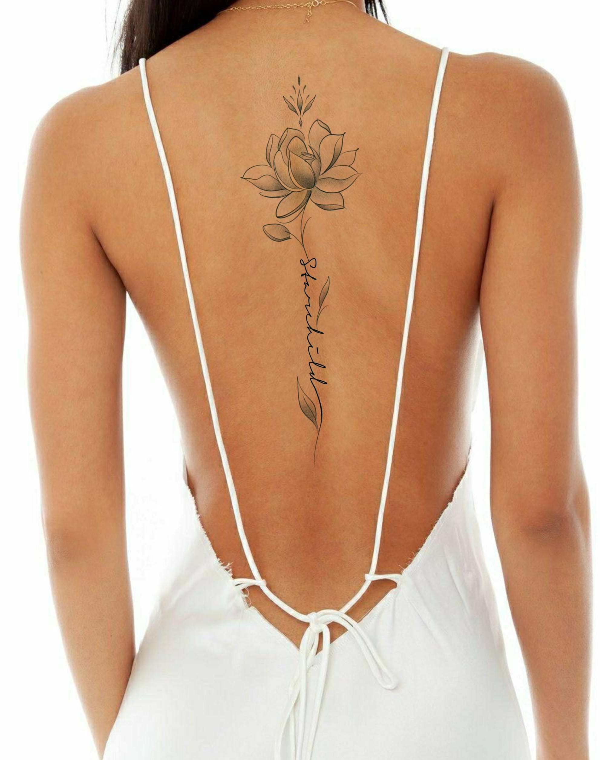 Graceful lines flow down the spine in this stunning lotus design, where delicate petals bloom above elegant script lettering. The minimalist black ink work creates a beautiful contrast against skin, with the vertical placement perfectly following the natural curve of the back—making it a showstopper for backless dresses and summer tops 🌸