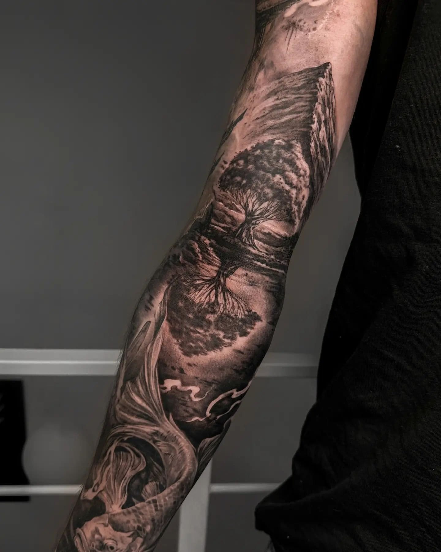 Masterful black and gray realism transforms this forearm into a living landscape where ancient trees seem to grow from beneath the skin. The intricate shading and organic flow create an almost three-dimensional effect, as if nature itself has claimed this canvas with windswept branches and textured bark that appears to move with every muscle flex 🌳