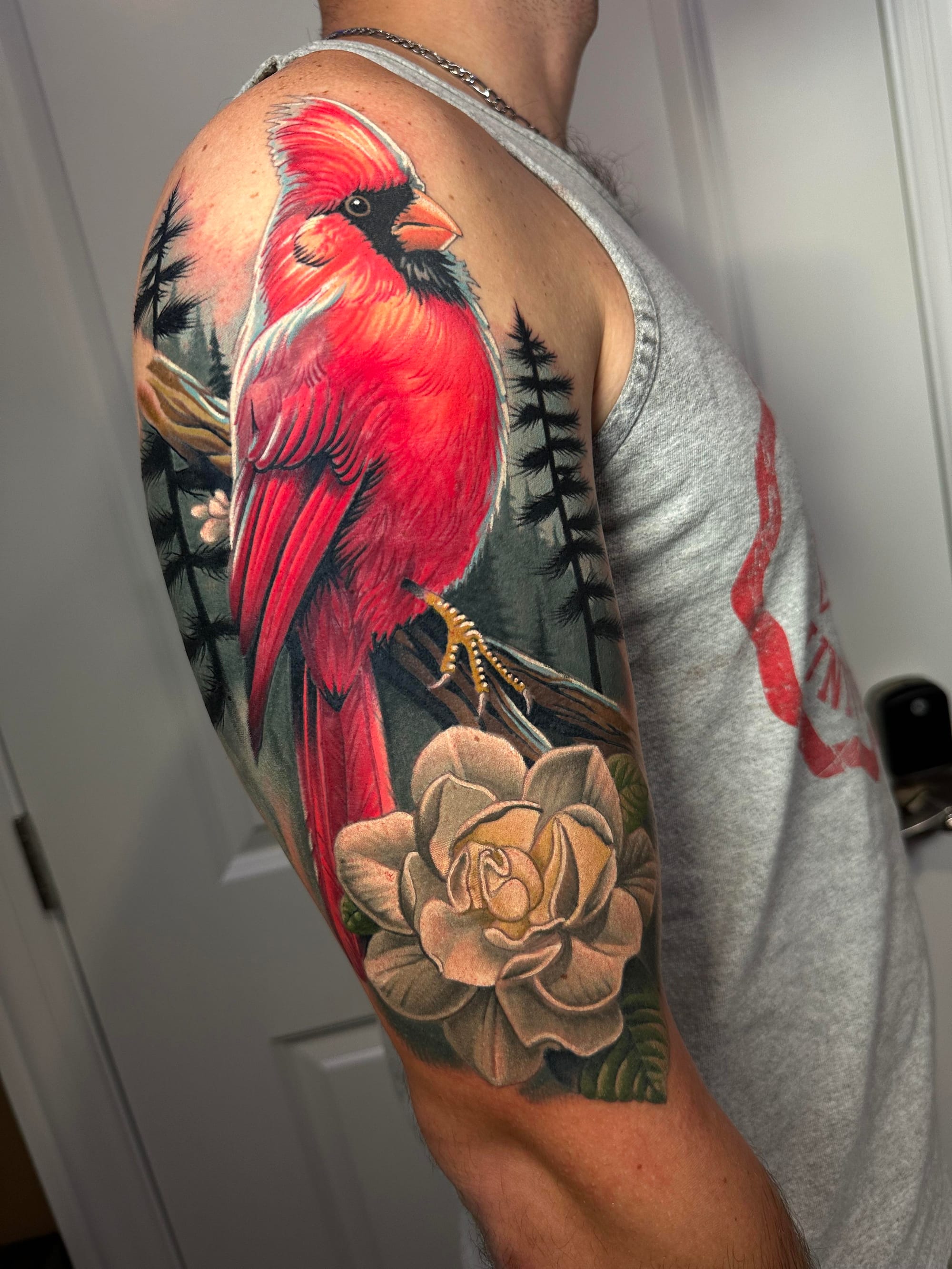 Vibrant crimson feathers cascade down this stunning half-sleeve, where a majestic cardinal perches among delicate evergreen branches and a beautifully shaded rose below. The realistic detail work is absolutely breathtaking - from the bird's distinctive black mask to the soft petals of the flower, every element flows seamlessly together in this nature-inspired masterpiece 🌹