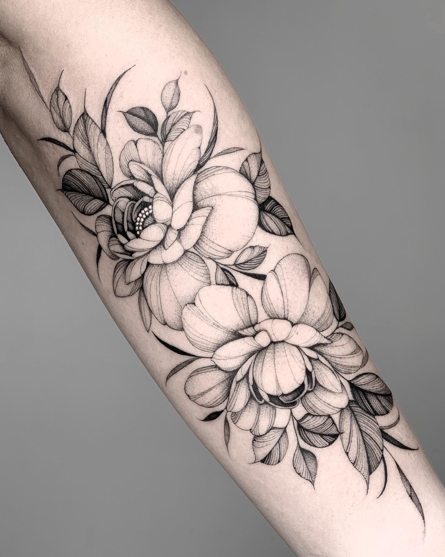 Delicate botanical artistry blooms across this forearm in stunning black and grey linework, featuring intricately detailed peonies and roses that seem to dance along the natural curves of the arm. The masterful shading and fine line technique creates incredible depth and dimension, while the organic flow of leaves and petals makes this piece feel like living art 🌸 Perfect placement that enhances the body's natural contours while showcasing the artist's exceptional skill in floral realism.