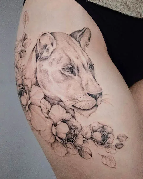 Graceful linework brings this majestic lioness to life on the thigh, her piercing gaze emerging from a cascade of delicate peonies and botanical elements. The artist's masterful use of fine line technique creates incredible depth and dimension, making the big cat appear almost three-dimensional against the skin 🌸 A stunning example of how black and grey realism can transform the body into a living canvas.