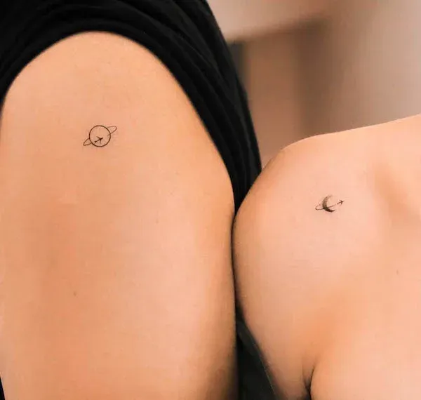 Minimalist magic comes alive in this adorable matching tattoo duo featuring a tiny planet with its delicate ring system paired with a crescent moon. The fine-line artistry and intimate placement on what appears to be arms or legs creates such a sweet celestial connection between two people ✨ Perfect proof that sometimes the smallest tattoos carry the biggest meaning about your cosmic bond together.