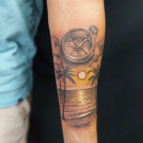 Wanderlust meets tropical paradise in this masterfully layered forearm piece, where a detailed vintage compass hovers above a golden sunset beach scene complete with swaying palms. The artist's skillful use of warm oranges and yellows creates a stunning contrast against the cool metallic tones of the navigational instrument above. Pure vacation vibes with deeper meaning about finding your true direction in life 🧭