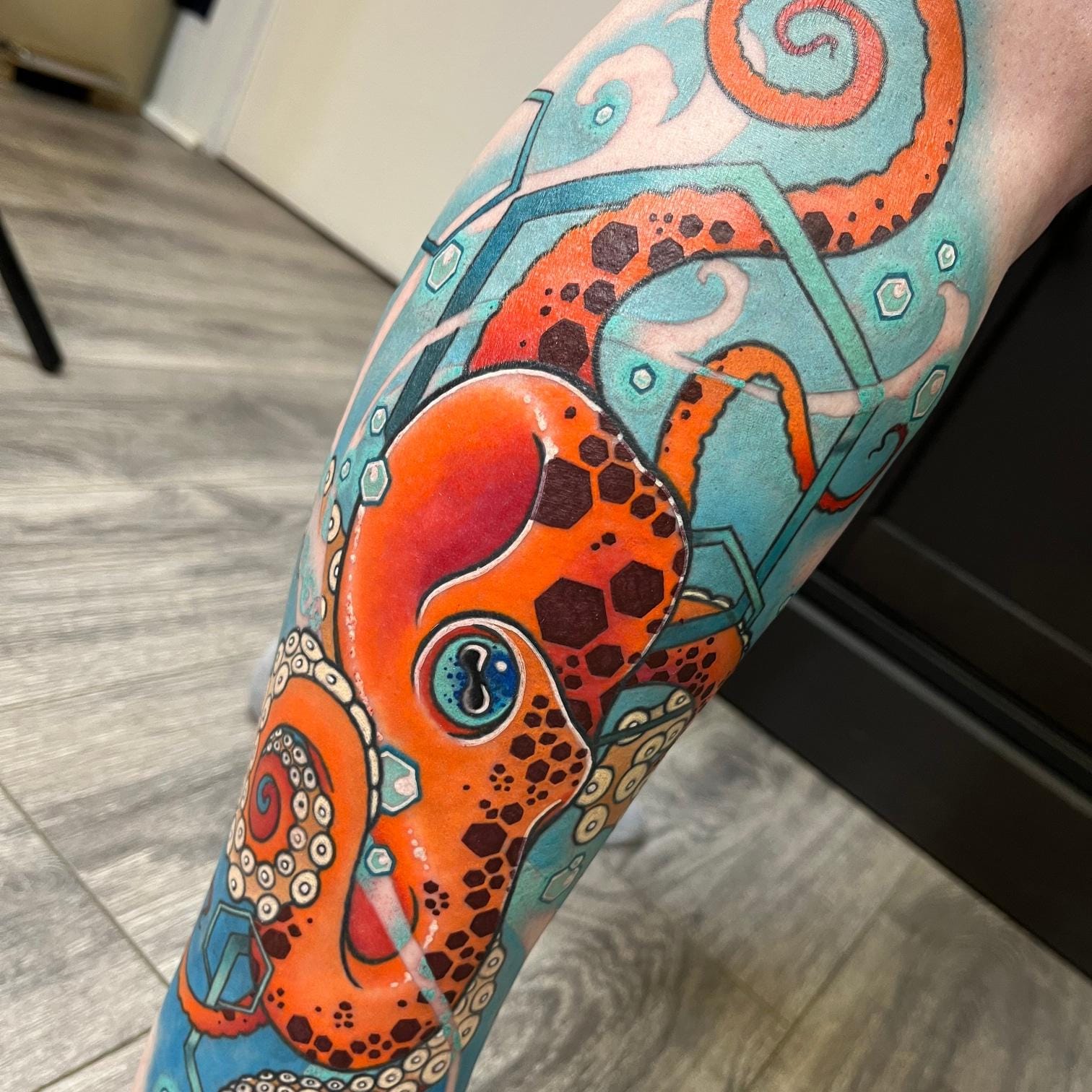 Vibrant coral and turquoise hues dance across this mesmerizing octopus leg tattoo, where geometric patterns seamlessly blend with organic tentacle forms. The artist's masterful use of negative space and bold color blocking creates a stunning underwater dreamscape that wraps beautifully around the calf. Notice how the creature's piercing blue eye serves as the perfect focal point amidst the swirling chaos of suction cups and crystalline details ✨