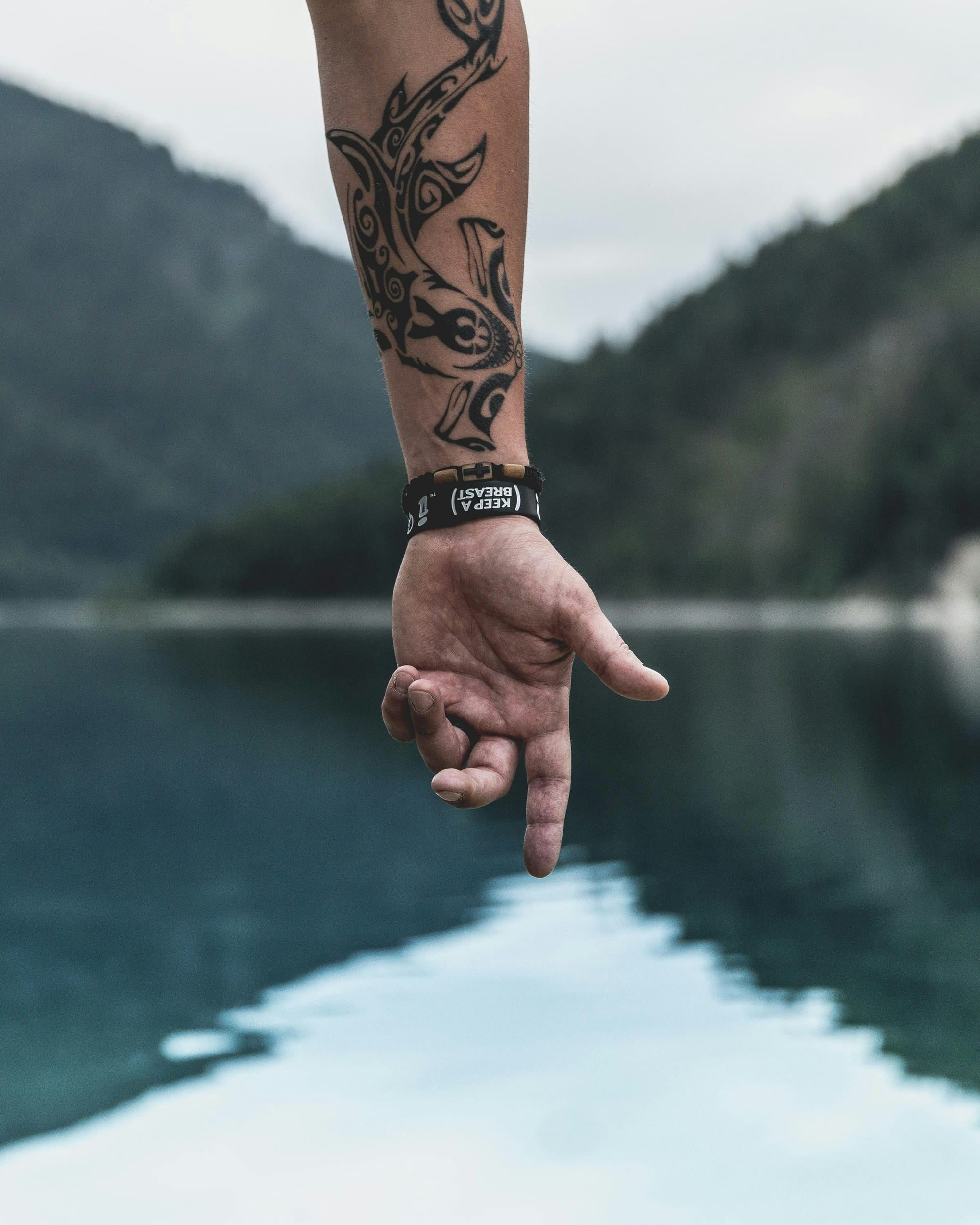 Ancient Celtic spirals dance down this forearm in bold black ink, creating a mesmerizing tribal design that flows like water against skin. The intricate knotwork and curved elements showcase traditional artistry with modern execution, while the scenic lakeside backdrop adds an ethereal quality to this powerful piece. ⚡