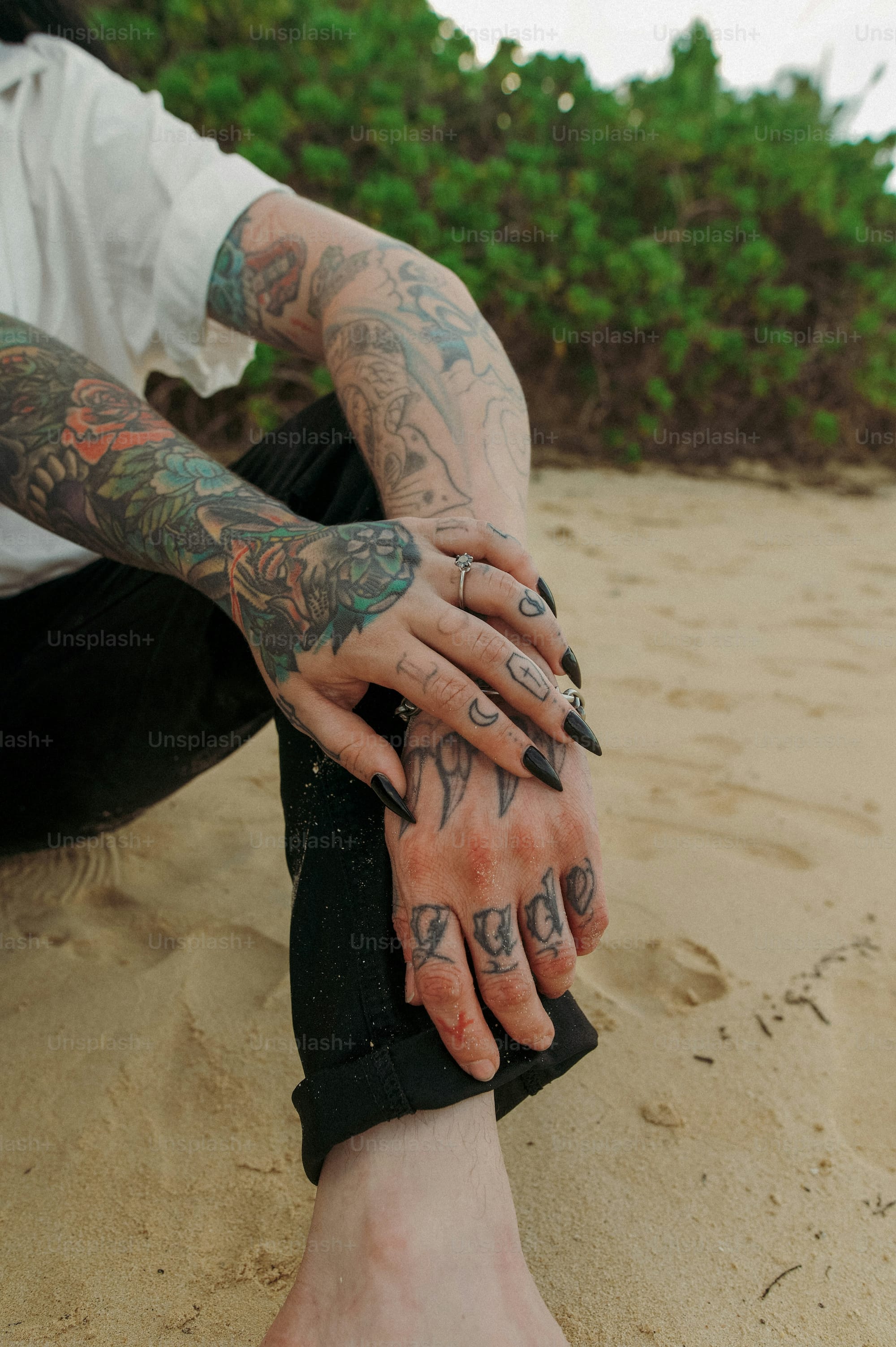 Intricate sleeve artistry cascades down both arms in this stunning display of botanical and mythical imagery, where vibrant greens and coral tones create a living canvas against sun-kissed skin. The juxtaposition of delicate finger lettering spelling 