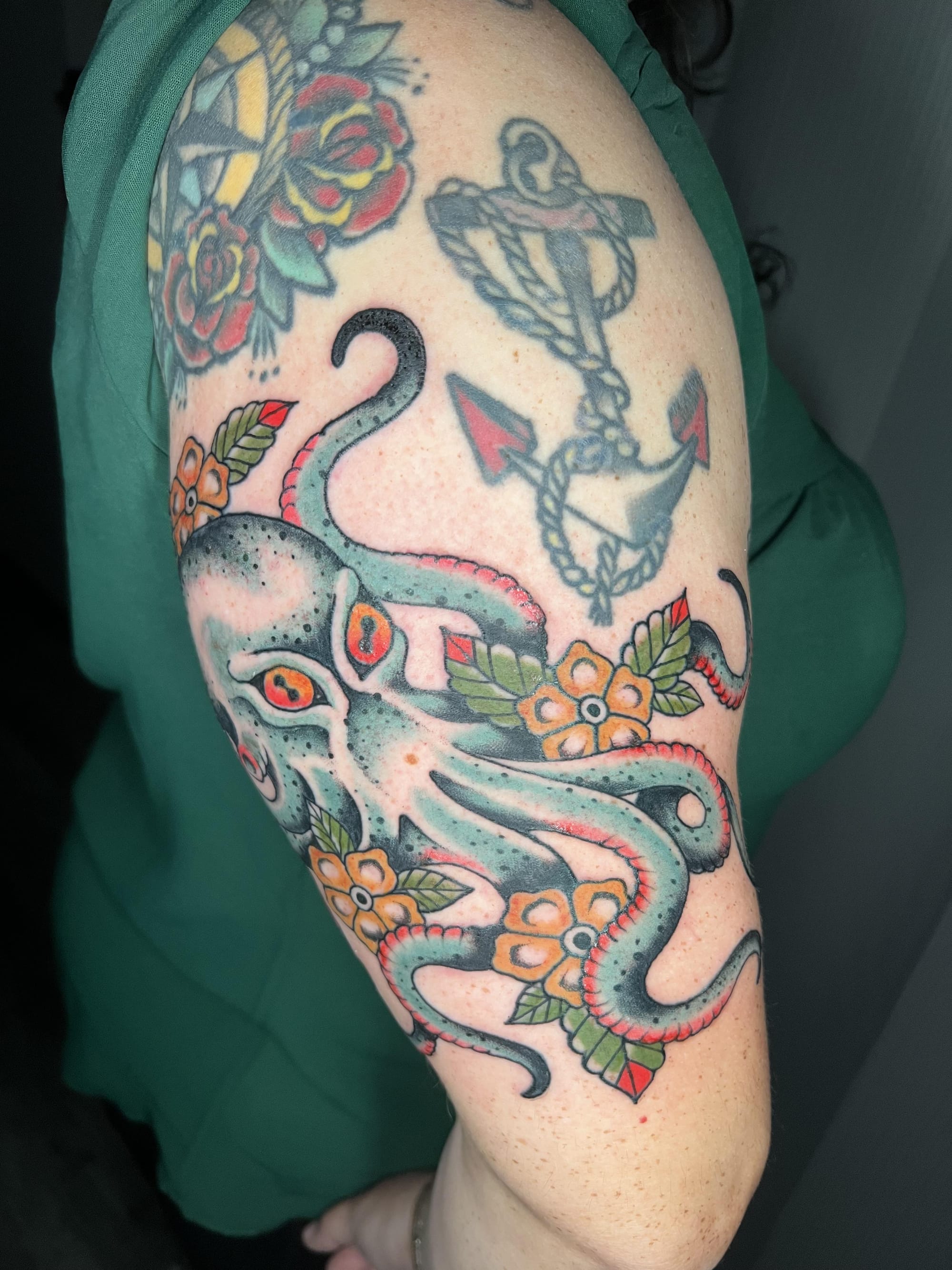 Serpentine grace meets nautical tradition in this stunning traditional-style half sleeve where a majestic octopus weaves between classic roses and a bold anchor. The artist's masterful use of teal and coral tones creates incredible depth while maintaining that timeless sailor tattoo aesthetic. Every tentacle curl and rope detail showcases the technical precision that makes traditional tattooing an enduring art form 🌊