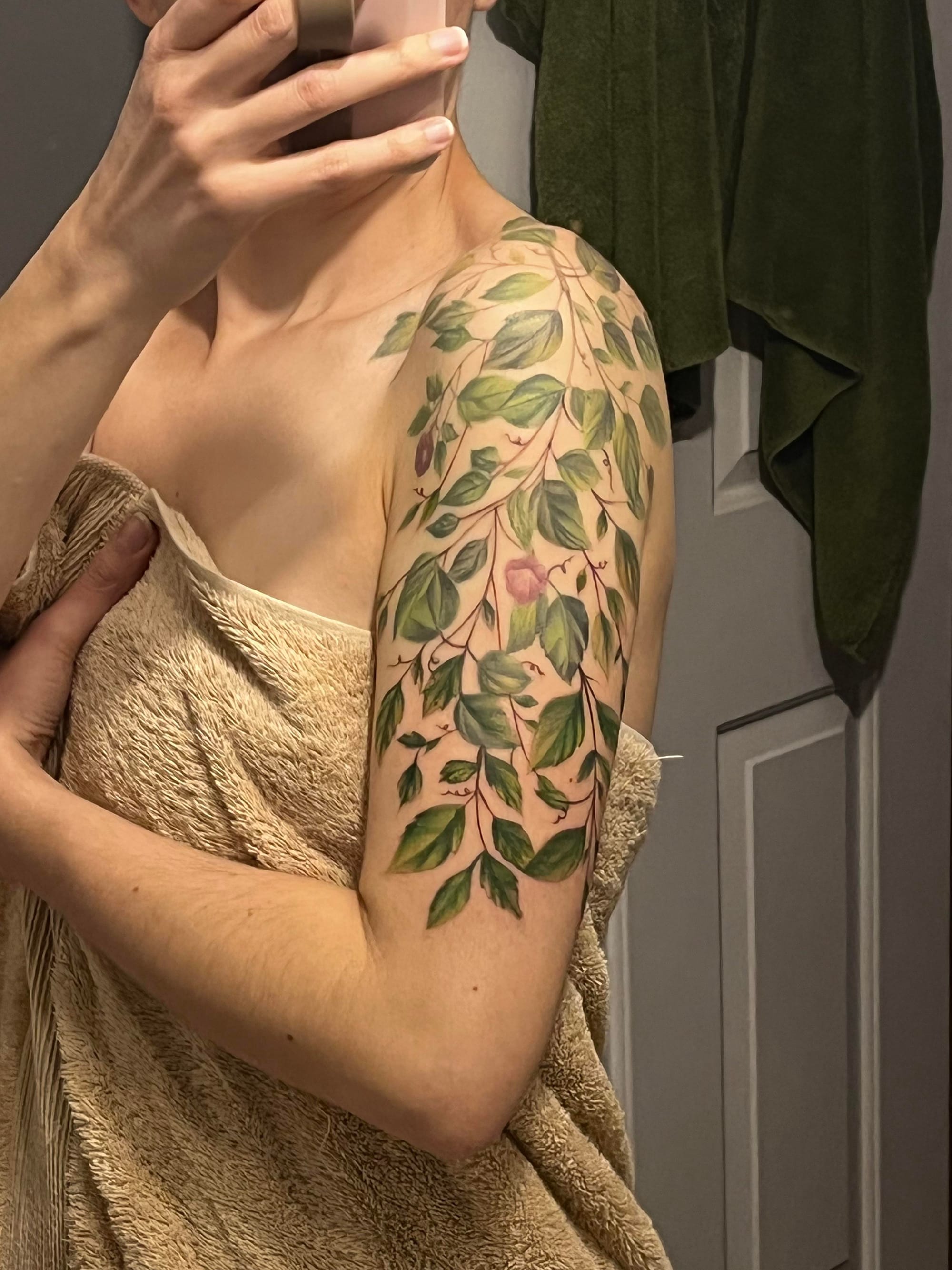 Botanical artistry cascades down this shoulder and upper arm like nature's own living jewelry, featuring delicate green leaves and soft pink blooms that seem to dance across the skin. The organic flow of this vine-inspired piece perfectly complements the body's natural curves, creating an elegant sleeve that whispers rather than shouts 🌿 The realistic shading and color work transforms this arm into a living garden that's both sophisticated and timelessly beautiful.
