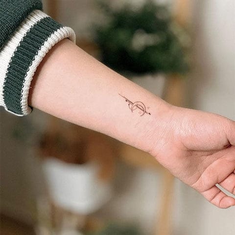 Delicate line work transforms a simple wrist placement into something truly special with this minimalist bow and arrow design. The fine black ink creates an elegant silhouette that follows the natural curve of the forearm, proving that sometimes the most understated tattoos make the strongest statement ✨