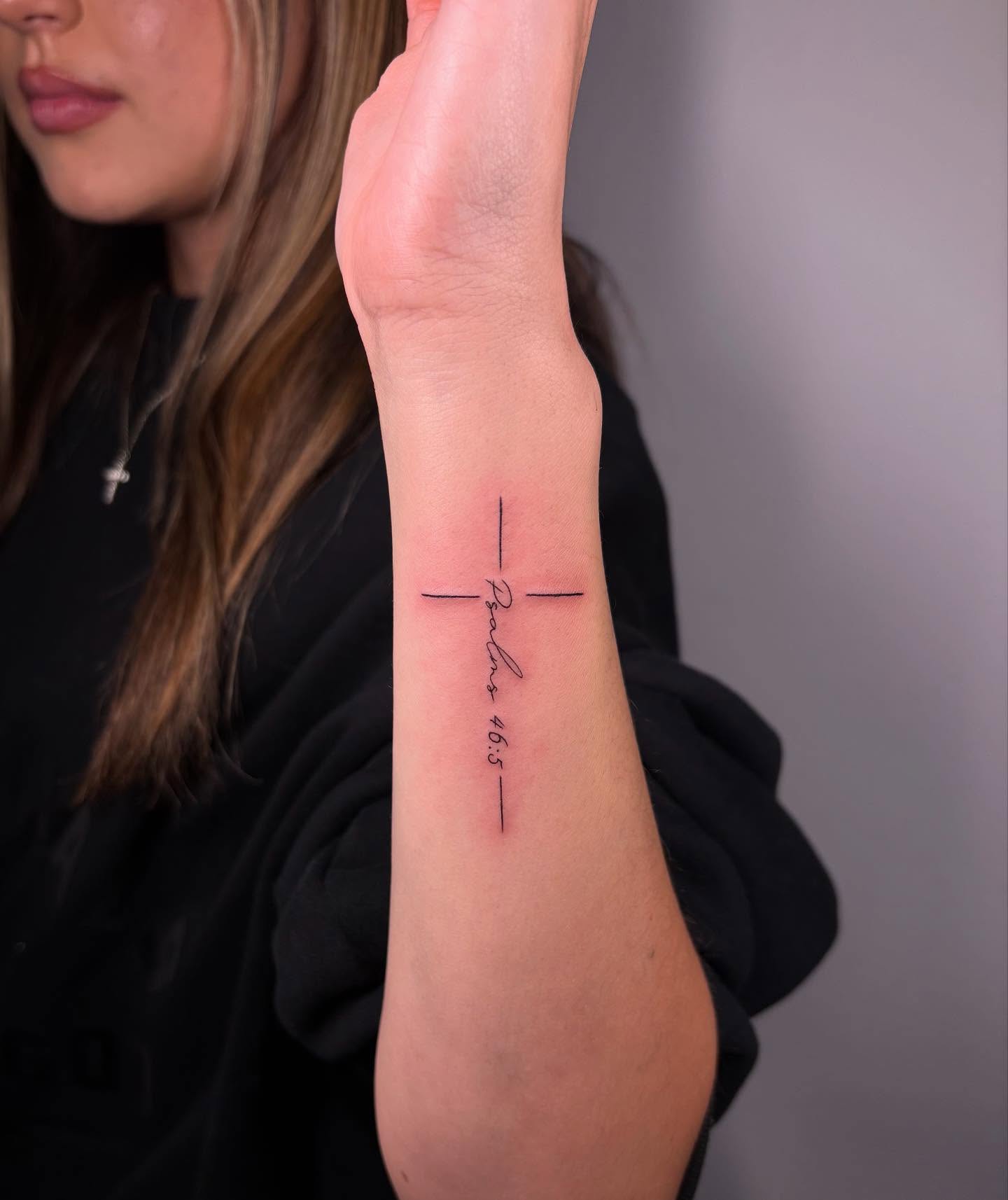 Delicate script cascades down this forearm like a prayer written in ink, forming an elegant cross where cursive meets clean lines ✨ The minimalist black design perfectly balances faith and artistry, creating a deeply personal statement piece that flows beautifully with the arm's natural contours.