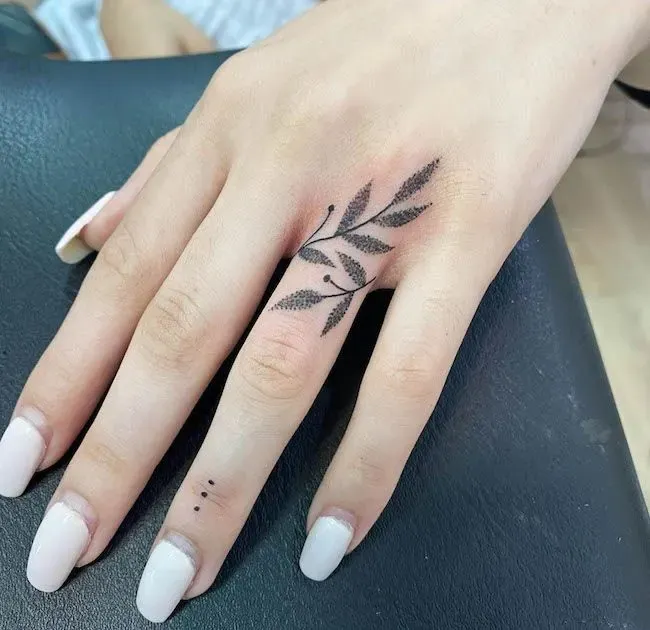 Delicate botanical artistry blooms across the knuckles in this stunning hand tattoo, where wispy leaves dance between the fingers in perfect black ink. The organic placement creates a natural flow that moves with the hand's gestures, while tiny dotwork details add an extra touch of feminine elegance 🌿