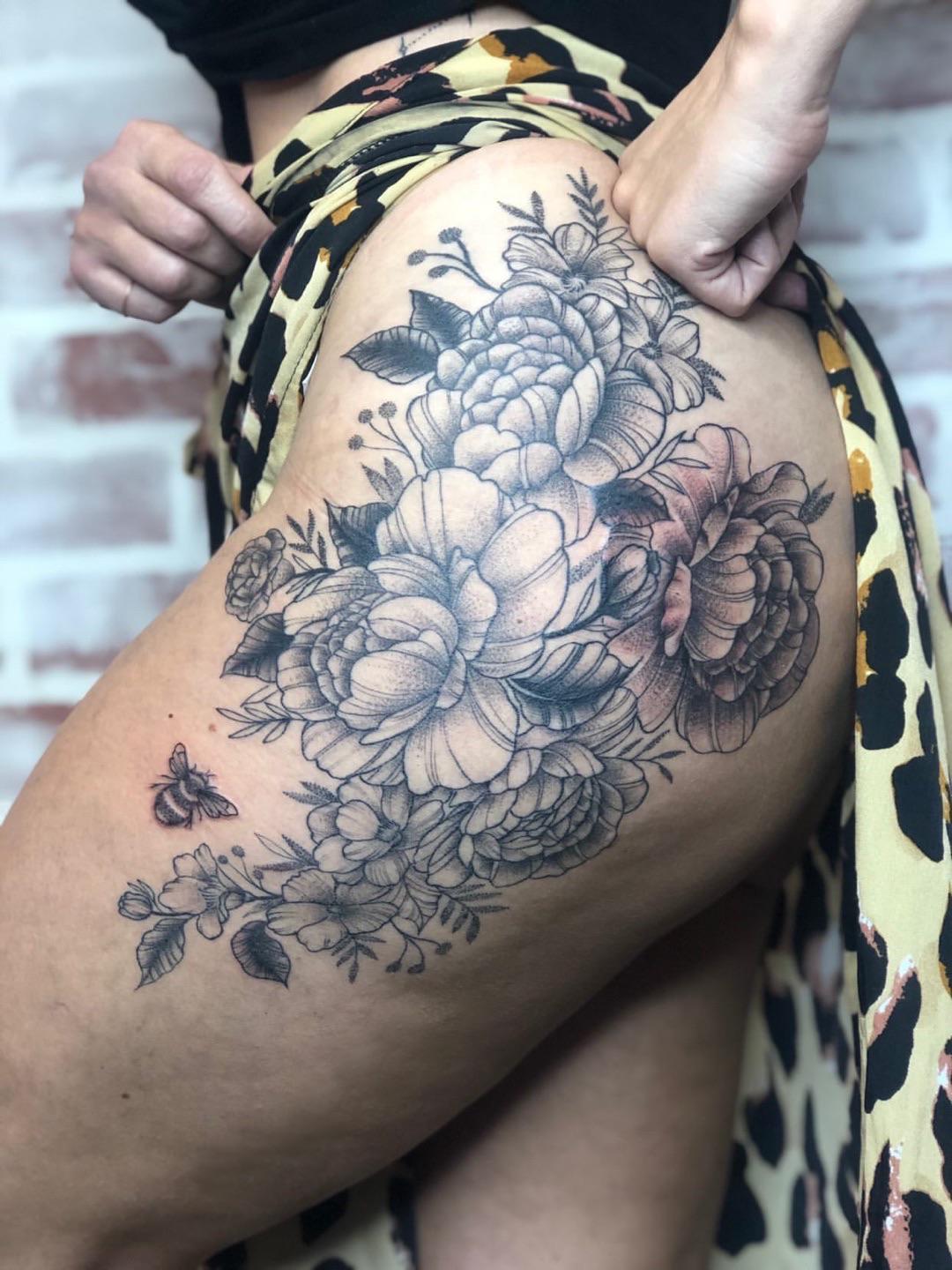 Cascading down the thigh like a botanical dream, this exquisite floral composition features intricately detailed peonies and roses rendered in stunning black and gray realism. The delicate shading and dimensional petals create an almost three-dimensional effect, while a tiny bee adds a whimsical touch to this garden masterpiece 🌸 The flowing arrangement perfectly complements the natural curves of the leg placement.