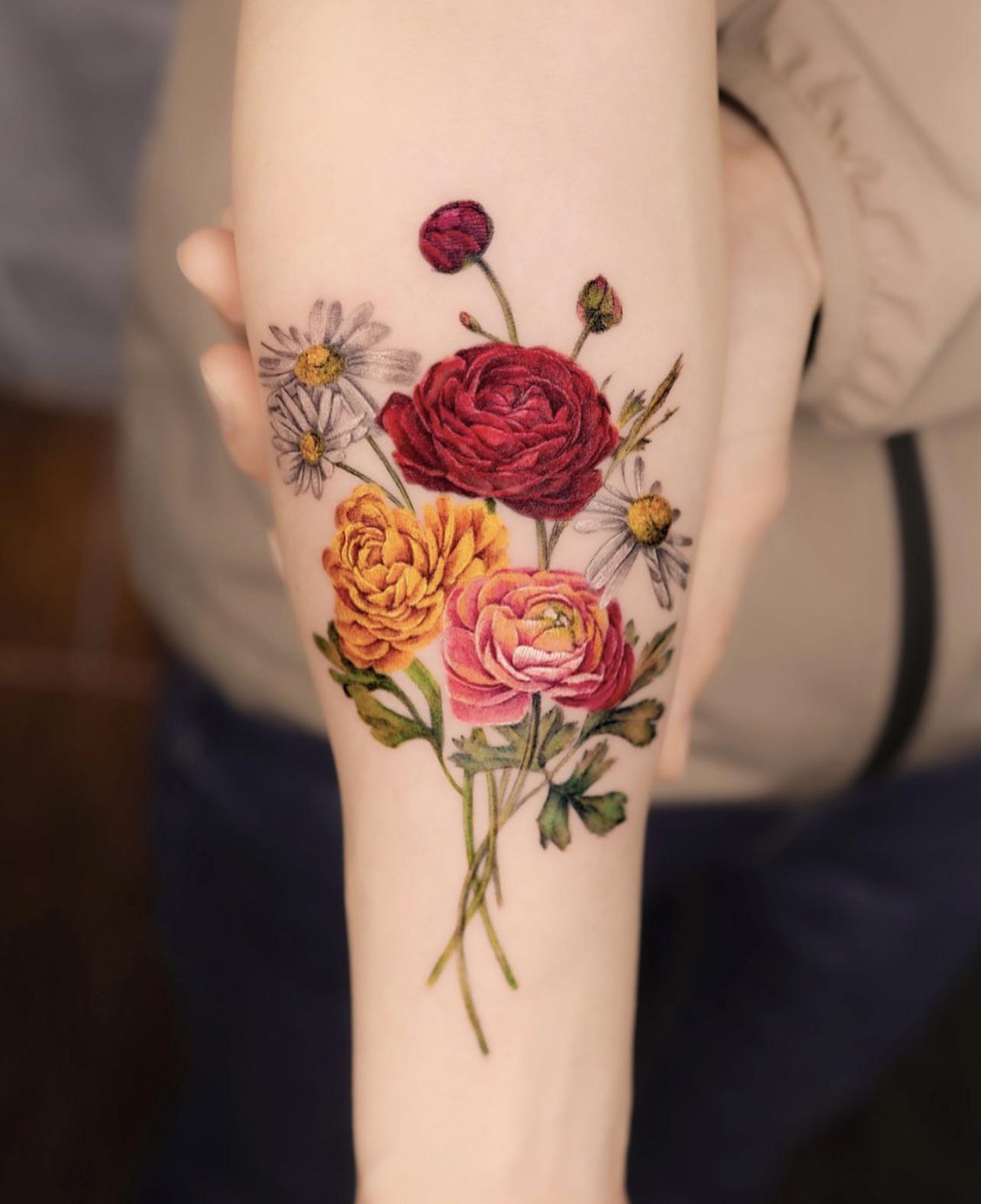 Botanical artistry blooms to life on this forearm canvas, where ranunculus flowers in deep burgundy, coral, and blush pink mingle with delicate white daisies in stunning realistic detail. The artist's masterful color saturation and precise shading technique transforms this floral bouquet into a living garden that seems to grow naturally along the arm's curve. 🌸