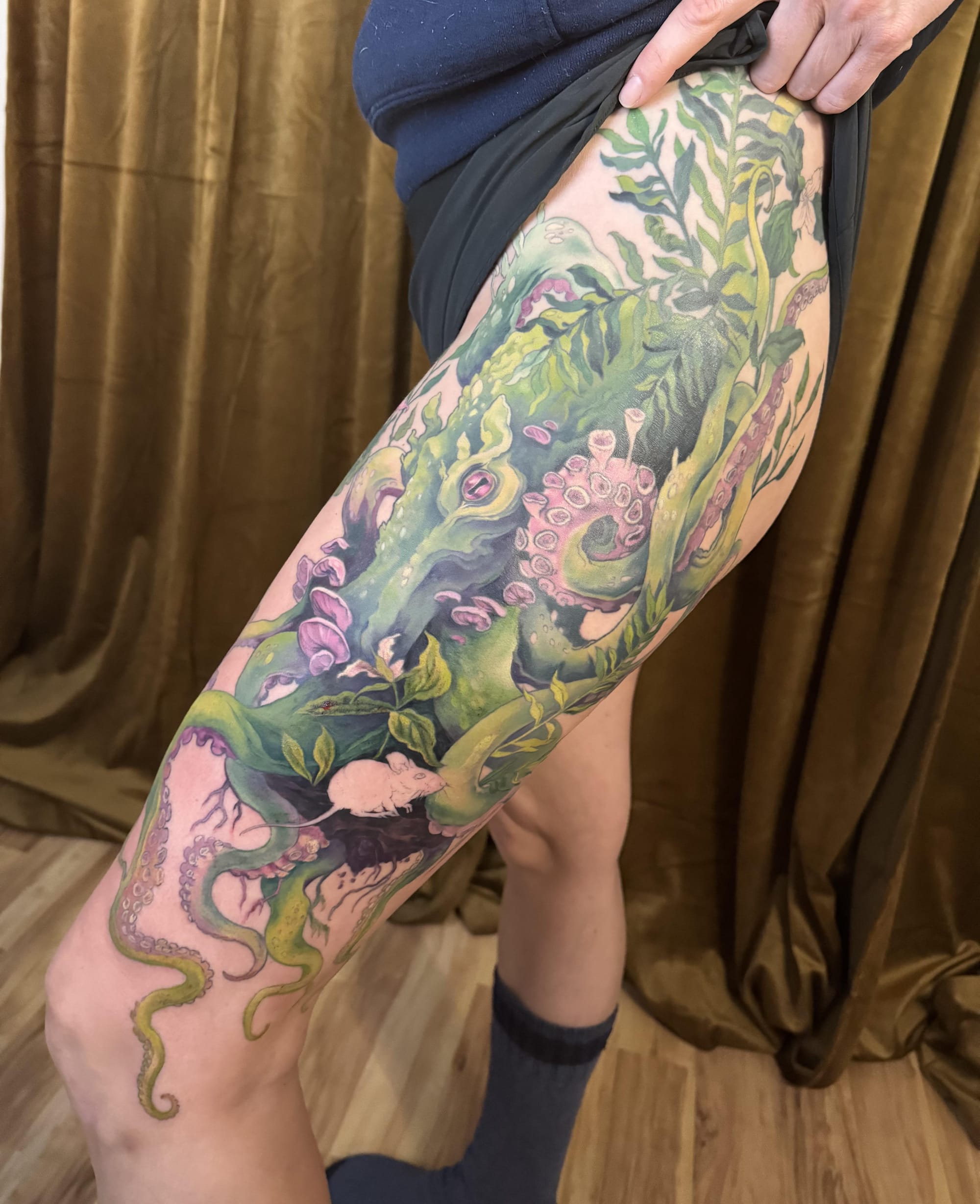 Botanical fantasy comes alive across this stunning leg piece, where a majestic green dragon emerges from lush foliage and delicate pink blossoms. The artist's masterful use of color creates incredible depth, with tentacle-like elements weaving through the composition to blur the lines between mythical creature and enchanted forest. 🐉 The flowing design perfectly follows the leg's natural curves, creating a living garden that seems to breathe with every movement.