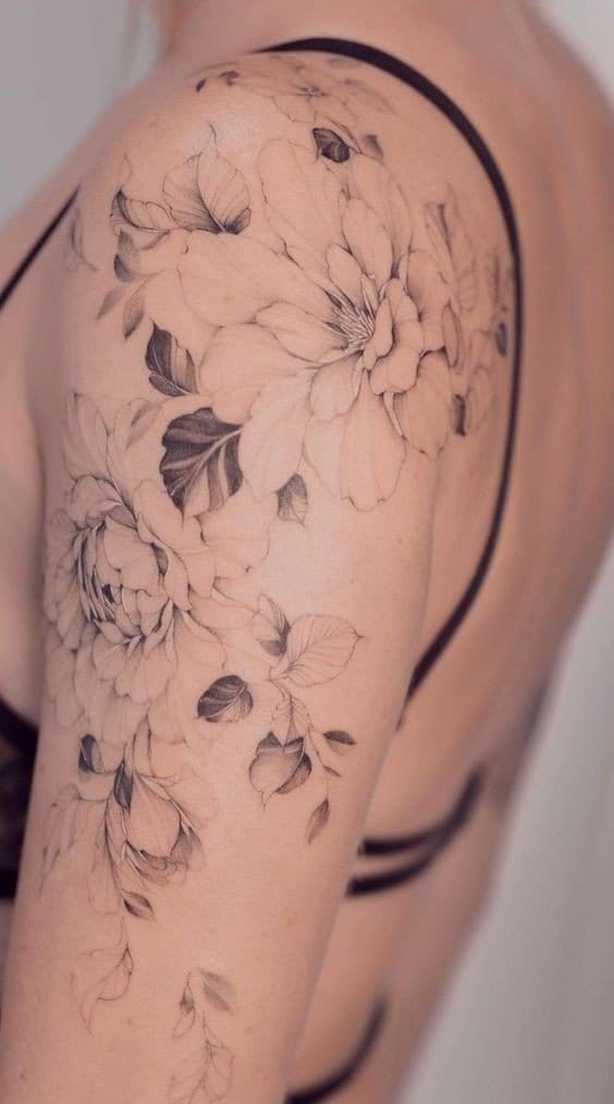 Cascading down the arm like a gentle waterfall, this botanical masterpiece features delicately shaded peonies and leaves that seem to dance across the skin. The soft black and grey linework creates an almost ethereal quality, while the flowing composition perfectly follows the natural curves of the shoulder and upper arm 🌸 A stunning example of how floral tattoos can be both feminine and bold.