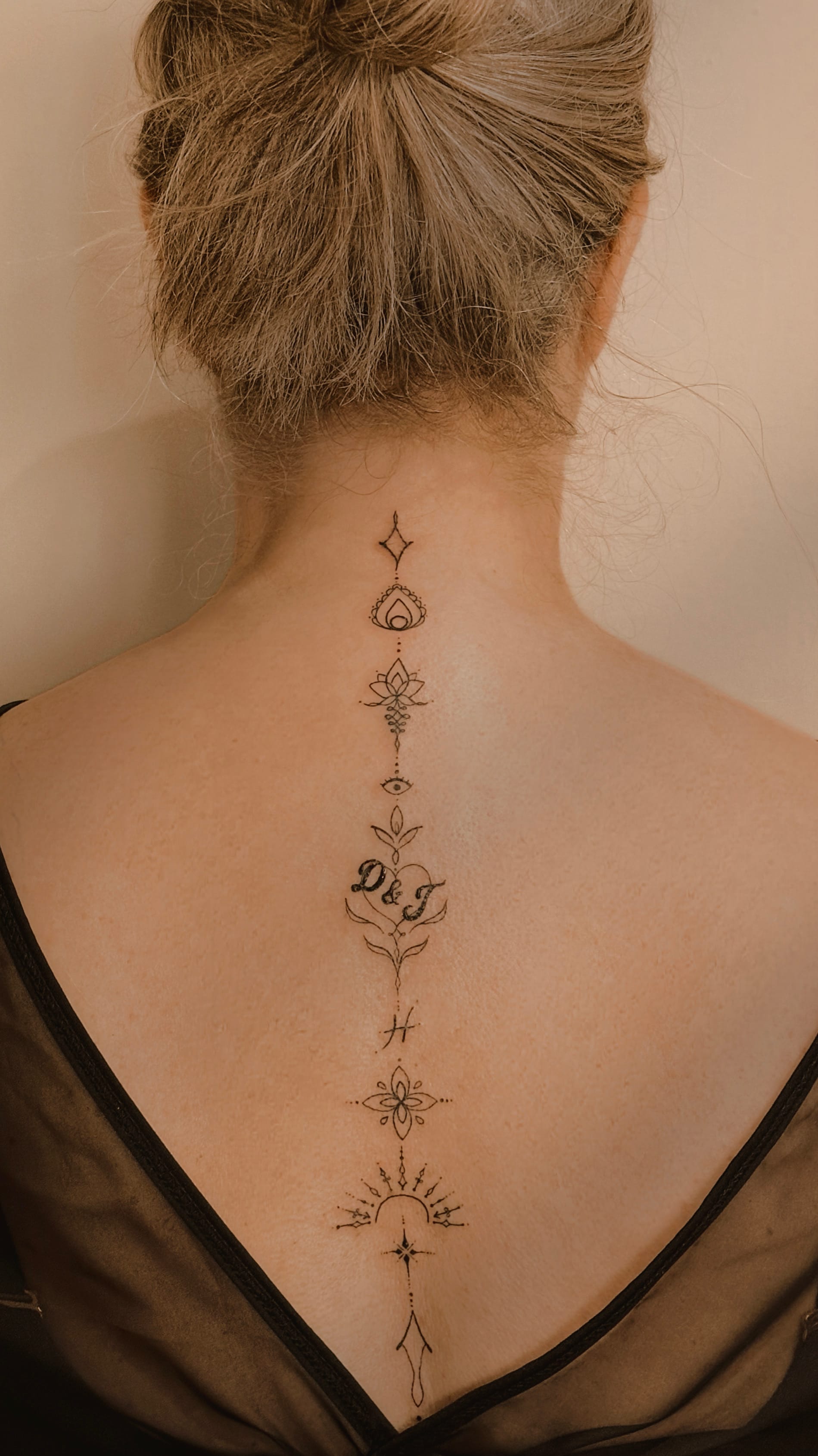 A delicate symphony of spiritual symbols flows down this spine like sacred poetry written in ink ✨ The intricate line work weaves together celestial stars, lotus blooms, mystical eyes, and ornate flourishes that create a mesmerizing vertical journey from nape to lower back. Each element seems to tell part of a deeper story about enlightenment and personal transformation, making this piece as meaningful as it is visually stunning.
