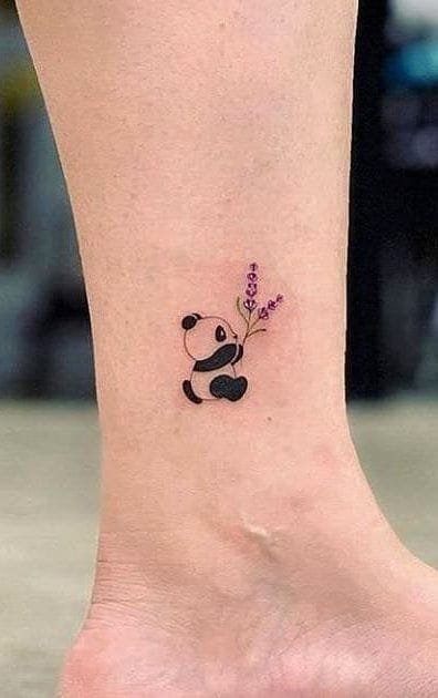 A delicate panda cradles purple lavender sprigs in this charming ankle tattoo that perfectly balances whimsy with botanical elegance. The minimalist black and white design gets a gentle pop of color from the soft purple flowers, creating a sweet nature-meets-cuteness vibe that's both playful and sophisticated 🐼