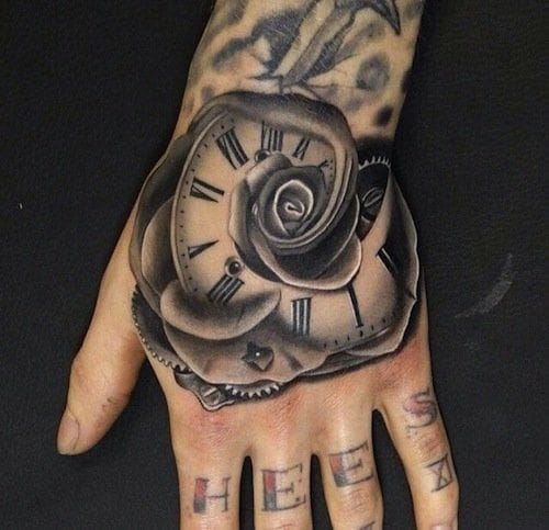 Mesmerizing black and gray artistry transforms this hand into a canvas where time literally blooms - a vintage clock face seamlessly morphs into rose petals, creating an optical illusion that's pure genius. The Roman numerals and intricate shading work make this piece feel like it belongs in a gothic romance novel, while the knuckle lettering adds that perfect rebellious touch ⏰