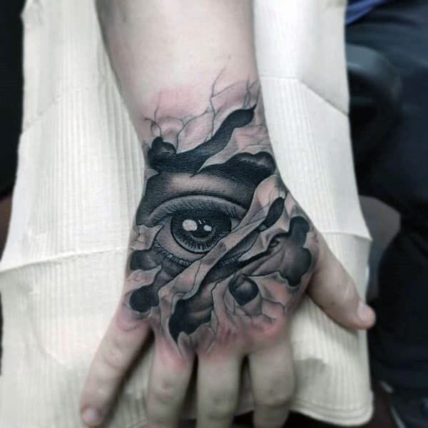 Dark artistry meets palm placement in this hauntingly beautiful hand tattoo featuring a realistic eye emerging from swirling smoke and shadowy depths. The monochromatic design creates incredible depth through expert shading techniques, transforming the hand into a mesmerizing canvas that seems to watch the world with mysterious intensity. 👁️ Perfect execution of difficult placement makes this piece both bold statement and artistic masterpiece.